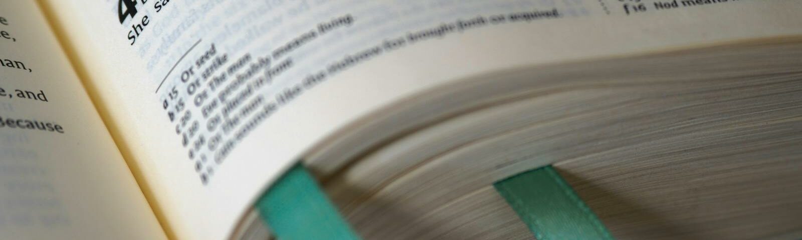Nyitott Biblia a Teremtés könyvével, Káin és Ábel történetével, teáskék könyvjelzőkkel.