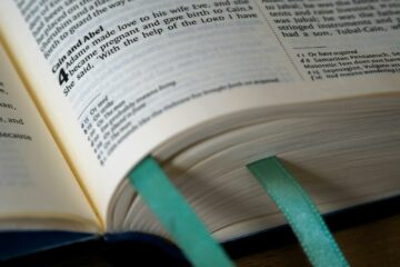 Nyitott Biblia a Teremtés könyvével, Káin és Ábel történetével, teáskék könyvjelzőkkel.